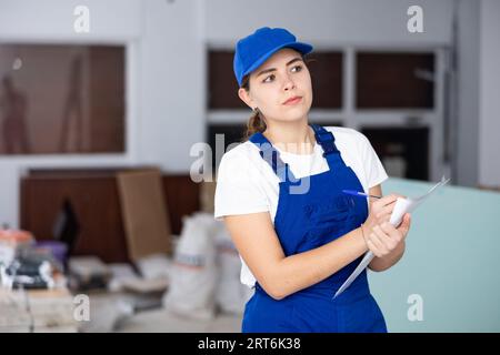 Fokussierte Bauherrin, die Papiere auf der Baustelle im Innenbereich ausfüllt Stockfoto