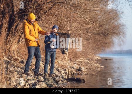 Vater und Sohn fischen an sonnigen Wintertagen. Sie haben einen Fisch gefangen und halten ihn in einem Landenetz. Stockfoto