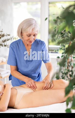 Professionelle Seniormasseuse bei der Anti-Cellulite-Oberschenkelmassage bei der jungen Frau Stockfoto