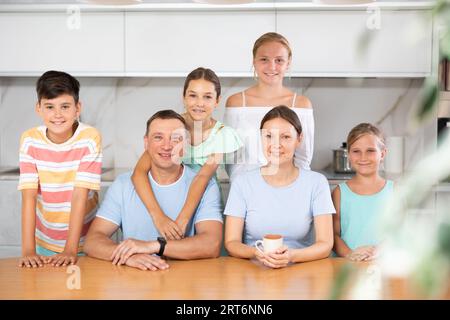 Glücklicher Vater und Mutter mit drei Töchtern und Sohn stehen neben dem Küchentisch. Stockfoto