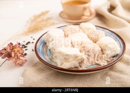 Traditionelle arabische Süßigkeiten Pishmanie und eine Tasse grüner Tee auf weißem Holzhintergrund und Leinentextilien. Seitenansicht, Nahaufnahme, selektiver Fokus. Stockfoto