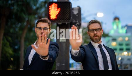Zwei gutaussehende Geschäftsleute im Anzug hören auf mit der Hand zu singen. Warnausdruck mit negativer und ernsthafter Geste im Gesicht. Halten Sie die Handbewegung an Stockfoto