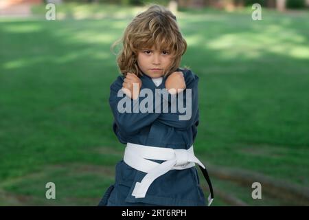 Ein Junge, der Karate im Freien trainiert. Sport-Karate-Kinder. Ein kleiner Junge mit Kimono, der Karate im Park macht. Sportkind mit Boxhandschuhen Trainingsbox Stockfoto