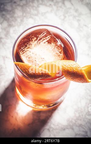 Hoher Winkel aus Glas, gefüllt mit altmodischen Cocktail- und Eiswürfeln, verziert mit Orangenschale auf Marmoroberfläche Stockfoto