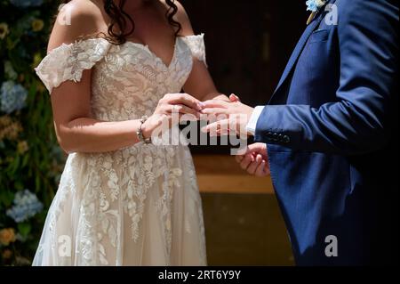 Anonymes Crop-Paar in schicken Hochzeitskleidern, das die Hände sanft hält, während es steht, und Ringe während der Hochzeitsfeier austauscht Stockfoto