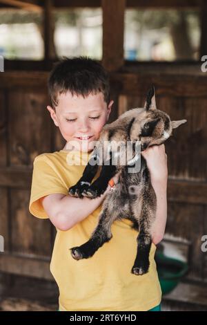 Porträt eines lächelnden Jungen in lässiger Kleidung, der während des Zoos süße junge amerikanische Pygmy hält Stockfoto