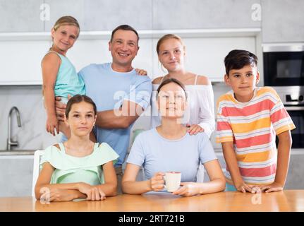 Glücklicher Vater und Mutter mit drei Töchtern und Sohn stehen neben dem Küchentisch. Stockfoto