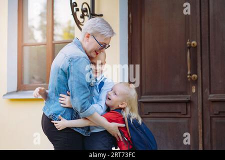 Mutter trifft Kinder aus der Schule. Kaukasischer Junge und Mädchen laufen auf ihre Mutter zu und umarmen sie. Stockfoto