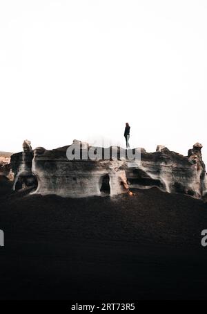 Minimalistisches vertikales Foto einer Touristenfrau, die auf dem Felsen in der Wüste steht. Stratifizierte Felsen (Teseguite - Lanzarote) mit Reisenden oben in d Stockfoto