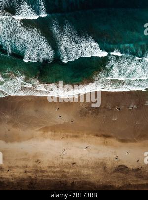 Vertikales Foto von gelbem Sandstrand mit Meer und Wellen - Blick von oben. Luftaufnahme des Strandes an sonnigen Tagen von oben. Stockfoto
