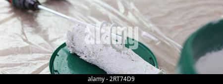 Lackmischer, Bürstenrolle und Eimer mit weißer Farbe auf überdachtem Boden. Stockfoto