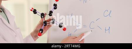 Chemikerin mit molekularem Modell und Zeichnen chemischer Formeln auf dem Whiteboard. Stockfoto