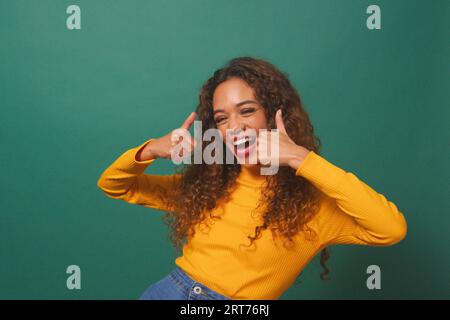 Schöne multiethnische Frau gibt doppelte Daumen nach oben, grüner Studiohintergrund Stockfoto