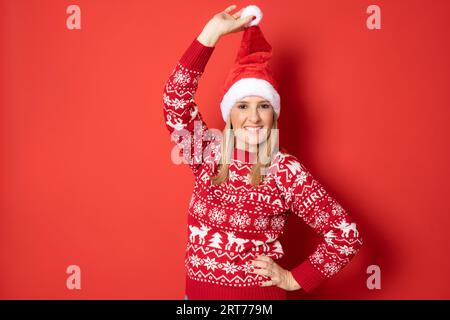 Glückliche junge Frau mit weihnachtsmannhut, die isoliert über rotem Hintergrund steht. Stockfoto