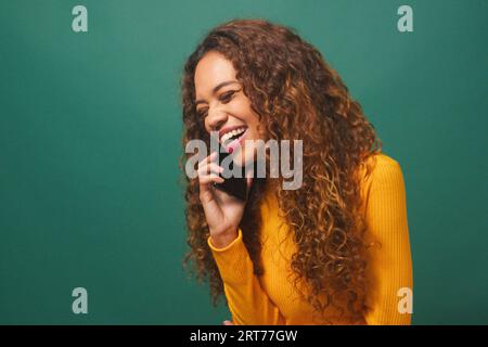 Glückliche schöne junge Frau redet und lacht auf Handy, grünes Studio Stockfoto