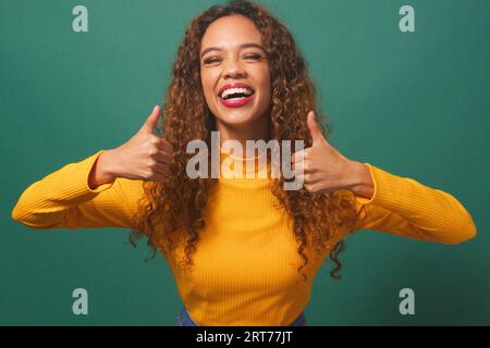 Schöne multiethnische Frau gibt doppelte Daumen nach oben, grüner Studiohintergrund Stockfoto