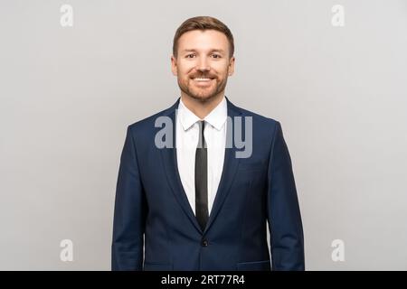 Lächelnder, selbstbewusster Geschäftsmann, der die Kamera isoliert auf grauem Studiohintergrund mit Kopierraum betrachtet Stockfoto