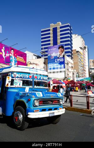 La Paz, BOLIVIEN; 11. September 2023: Ein Vintage-Kleinbus für öffentliche Verkehrsmittel vor einer Horde mit dem bolivianischen Präsidenten Luis Arce Catacora, der die "Industrialisierung von Lithium, einen großen Schritt in Richtung einer nachhaltigen Zukunft für Bolivien" im Zentrum von La Paz fördert. Bolivien verfügt über einige der größten Lithiumreserven der Welt in der Salar de Uyuni-Saline, deren Entwicklung für die Wirtschaftspolitik der Regierung von zentraler Bedeutung ist. In diesem Jahr hat Bolivien Vereinbarungen mit dem chinesischen Batteriehersteller CATL und der Citic Guoan Group sowie dem russischen Staatsunternehmen Rosatom als Partner zur Entwicklung dieser Ressourcen unterzeichnet. Stockfoto