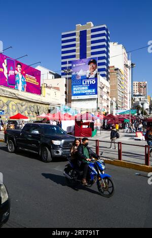 La Paz, BOLIVIEN; 11. September 2023: Ein Paar auf einem Motorrad ohne Helme vor einer Hortung mit dem bolivianischen Präsidenten Luis Arce Catacora, der die "Industrialisierung von Lithium, einen großen Schritt in Richtung einer nachhaltigen Zukunft Boliviens" in La Paz fördert. Bolivien verfügt über einige der größten Lithiumreserven der Welt in der Salar de Uyuni-Saline, deren Entwicklung für die Wirtschaftspolitik der Regierung von zentraler Bedeutung ist. In diesem Jahr hat Bolivien Vereinbarungen mit dem chinesischen Batteriehersteller CATL und der Citic Guoan Group sowie dem russischen Staatsunternehmen Rosatom als Partner zur Entwicklung dieser Ressourcen unterzeichnet. Stockfoto