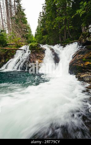 Starker Gebirgswasserfall im grünen Wald – vertikale Weitwinkelaufnahme. Wunderschöner und kraftvoller Wasserfall mit türkisfarbenem Wasser - Steine und Felsen Stockfoto