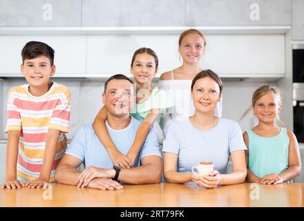 Glücklicher Vater und Mutter mit drei Töchtern und Sohn stehen neben dem Küchentisch. Stockfoto
