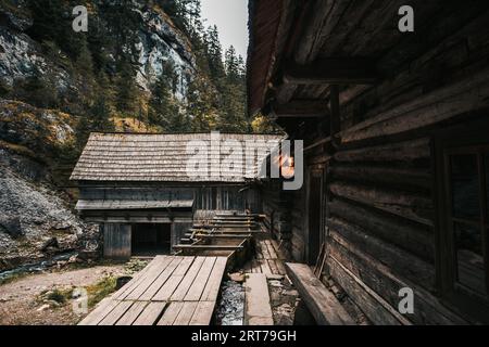Wunderschöne alte Holzhütte tief im Wald - Mlyny Oblazy (Slowakei). Alte Holzmühle mit Felsen im Hintergrund im Herbst. Stockfoto