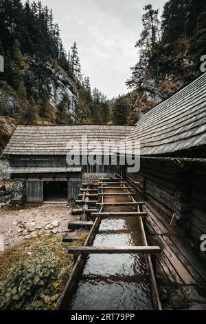 Vertikales Foto einer wunderschönen Holzhütte tief im Wald - Mlyny Oblazy (Slowakei). Alte Holzmühle mit Felsen im Hintergrund im Herbst. Stockfoto