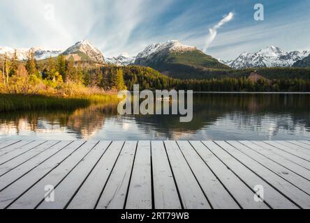 Maulwurf (Pier) auf dem See in Herbstlandschaft mit schönen und verschneiten Bergen im Hintergrund. Strbske pleso in der Hohen Tatra im Herbst mit Holzmole und Stockfoto