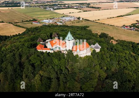 Luftbild des märchenhaften Schlosses Smolenice in den Bergen der Kleinen Karpaten - natürliches Sonnenlicht. Foto von oben über dem Schloss auf dem Hügel mit Dorf Stockfoto