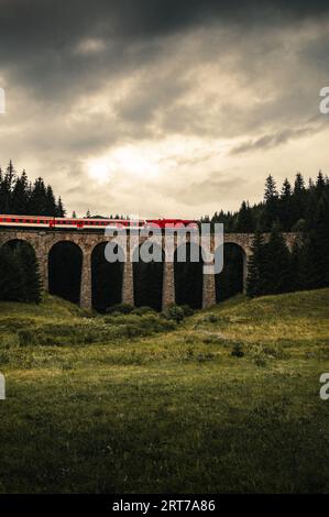 Vertikales Foto des Zuges auf einem Viadukt im Wald von Telgart-Slowakei mit stimmungsvollem und dramatischem Himmel vor Sturm. Stockfoto