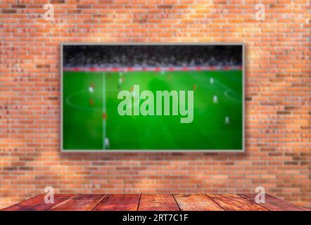 Ein Fernseher mit Fußballfeld an der Backsteinwand und Holztisch mit leerem Platz in selektivem Fokus Stockfoto