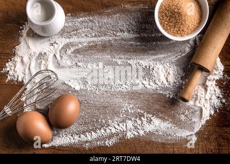 Weizenmehl, Zucker, Stecknadel und Schneebesen auf hölzernem Hintergrund, Draufsicht, Kopierraum. Zutaten für Bäckerei, Backen oder Kochkonzept. Stockfoto