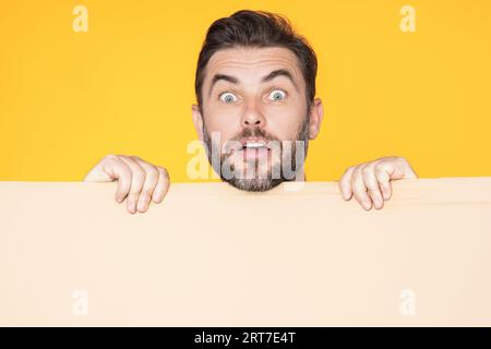 Erstaunter Kerl mit leerer Werbebanner isoliert im Studiohintergrund. Porträt eines überraschten Mannes mit leerem Plakat. Erstaunter Mann, der ein leeres Poster zeigt Stockfoto