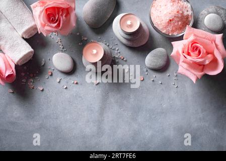Spa- und Wellnesskonzept. Rosa Rosenblüten, Massage Zen Steine und Kerzen auf grauem Betonhintergrund, Kopierraum. Stockfoto