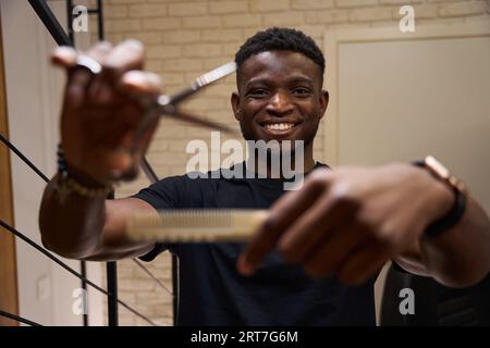 Der afroamerikanische Friseur steht mit Schere und Kamm am Arbeitsplatz Stockfoto