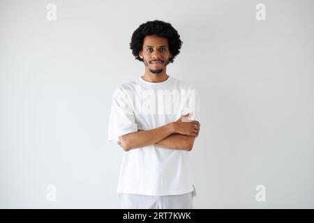 Porträt des lächelnden, selbstbewussten, jungen Schwarzen Mannes, der mit gekreuzten Armen steht Stockfoto