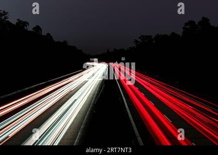 Leichte Autowege. Lichter auf der Autobahn. Spuren von Autos. Abstraktes Licht, Lichtschweife. Highway bei Sonnenuntergang und viel Verkehr. Autobahn bei Nacht. Stockfoto