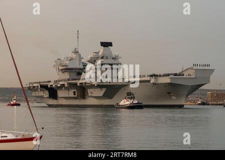 Portsmouth, England, Großbritannien. 8. September 2023. Die HMS Queen Elizabeth verlässt den Hafen von Portsmouth in der Abenddämmerung mit einer Eskorte von Schleppern und Sicherheitsvessen Stockfoto