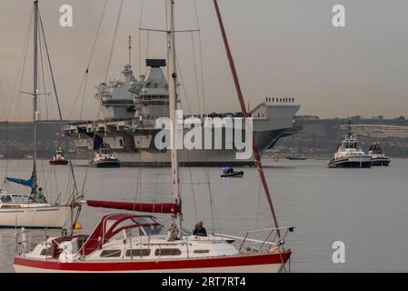 Portsmouth, England, Großbritannien. 8. September 2023. Die HMS Queen Elizabeth verlässt den Hafen von Portsmouth in der Abenddämmerung mit einer Eskorte von Schleppern und Sicherheitsvessen Stockfoto