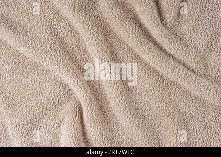 Frottee, beigefarbener Handtuchhintergrund. Zerknittertes und zerknittertes, weiches, flauschiges Textil-Bad- oder Strandhandtuchmaterial. Draufsicht, Nahaufnahme. Stockfoto