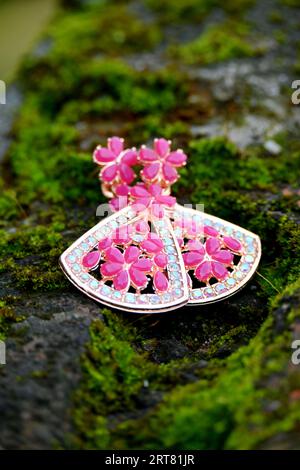 Schließen Sie das Paar rosa silberfarbene Ohrringe auf dem grünen Gras Soft Focus natürlichen grünen braunen Hintergrund. Stockfoto