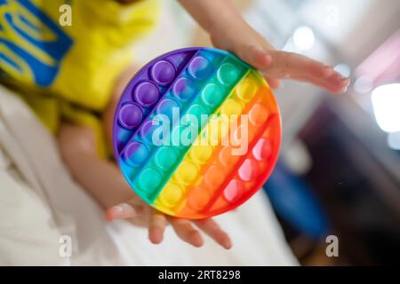 Die Hände des Kleinkindes halten ihn fest. Ein fröhliches Kind auf dem Bett mit einem Anti-Stress-Spielzeug. Weiche Stofftiere mit Blasen. Kind spielt mit Stockfoto