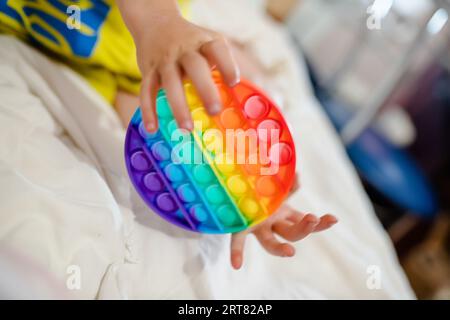 Die Hände des Kleinkindes halten ihn fest. Ein fröhliches Kind auf dem Bett mit einem Anti-Stress-Spielzeug. Weiche Stofftiere mit Blasen. Kind spielt mit Stockfoto