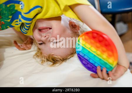 Weiche Stofftiere mit Blasen. Das Kind spielt mit dem Regenbogenpop-it in Form eines Kreises Stockfoto