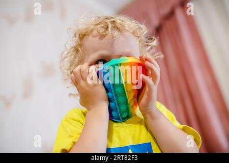 Weiche Stofftiere mit Blasen. Das Kind spielt mit dem Regenbogenpop-it in Form eines Kreises Stockfoto