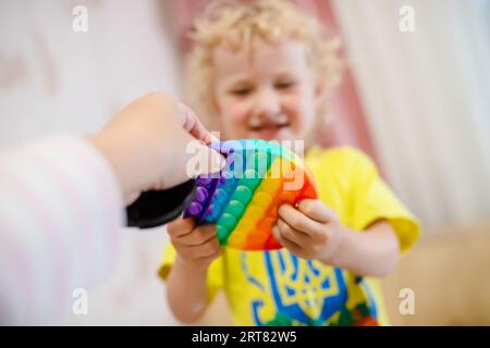 Blondes Mädchen, das mit Pop-it-Sinnesspielzeug spielt. Ein modisches Silikonspiel für gestresste Kinder und Erwachsene. Weiche Stofftiere mit Blasen. Kind spielt Stockfoto