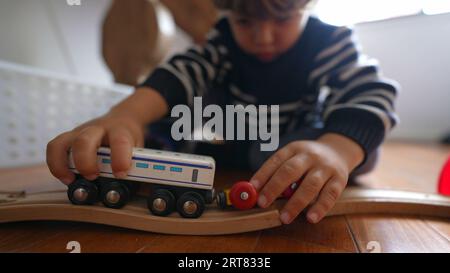 Kind spielt zu Hause mit Spielzeug, Nahaufnahme kleiner Junge spielt mit traditionellen Retro-Eisenbahnwaggons auf Holzschienen Stockfoto