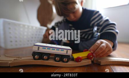 Kind spielt zu Hause mit Spielzeug, Nahaufnahme kleiner Junge spielt mit traditionellen Retro-Eisenbahnwaggons auf Holzschienen Stockfoto