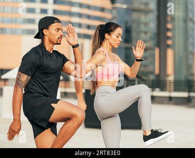 Seitenansicht von zwei Personen in Fitnesskleidung, die gemeinsam auf dem Dach springen. Junge Fitnesssportler, die Aufwärmübungen machen. Stockfoto