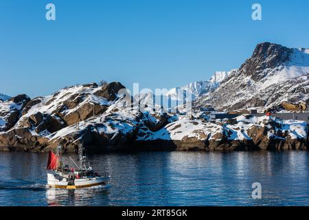 Kleines Fischerboot bei Svolvaer auf den Lofoten Inseln in Norwegen mit Schnee am klaren Tag mit blauem Himmel Stockfoto